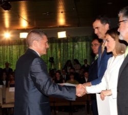 Uno de los becados recibe el saludo y el diploma de Sus Majestades los Reyes.