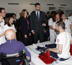 Sus Majestades los Reyes conversan con un paciente en una de las camas de tratamiento de rehabilitación de la sala de fisioterapia