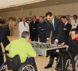 Sus Majestades los Reyes juegan al futbolín con unos usuarios del centro en sillas de ruedas