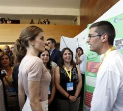Su Majestad la Reina frente a uno de los paneles informativos conversa con uno de los jóvenes participantes