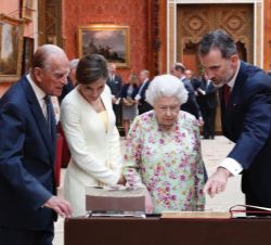Sus Majestades los Reyes con Su Mjestad la Reina Isabel II y Su Alteza Real el Duque de Edimburgo comentan una de las piezas expuestas