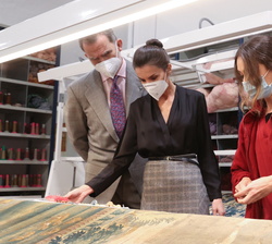 Sus Majestades los Reyes observan la restauración de un tapiz en rulo