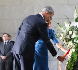 Sus Majestades los Reyes se acercan a la corona para arreglar la cinta 