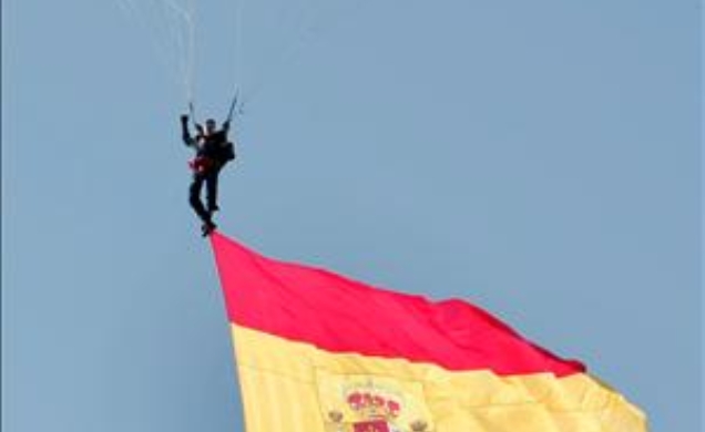 Uno de los miembros de la Patrulla Acrobática Paracaidista del Ejército del Aire (PAPEA) hace ondear la bandera española en el cielo de Madrid, durant