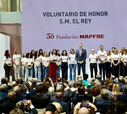 Su Majestad el Rey en el escenario junto a una representaión de los voluntarios que colaboran con la Fundacióbn MAPFRE