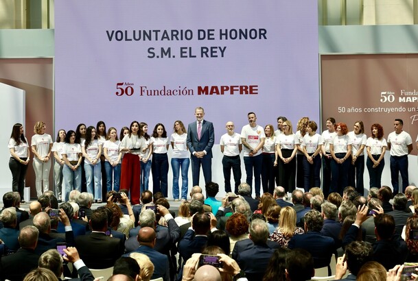 Su Majestad el Rey en el escenario junto a una representaión de los voluntarios que colaboran con la Fundacióbn MAPFRE