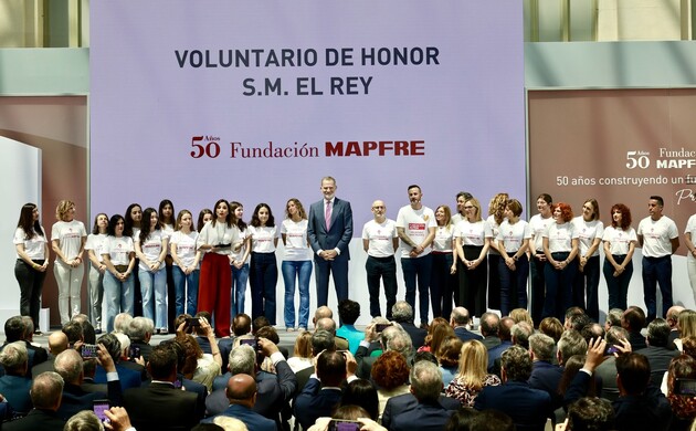 Su Majestad el Rey en el escenario junto a una representaión de los voluntarios que colaboran con la Fundacióbn MAPFRE