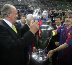 Don Juan Carlos sostiene el trofeo de campeón con el capitán del F.C. Barcelona, Carles Puyol, en presencia del presidente del club, Joan Laporta
